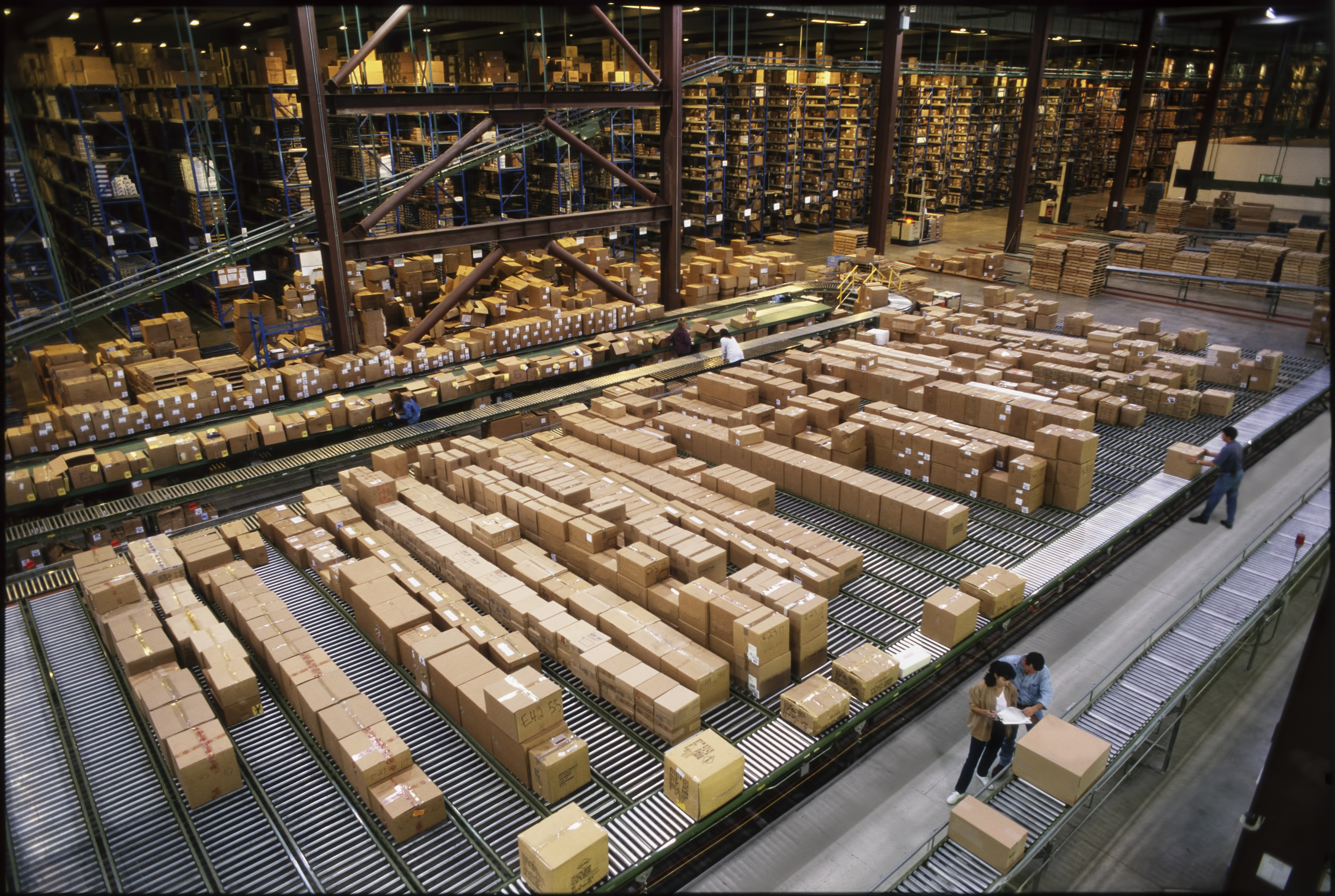 Overview of a large industrial distribution warehouse storing products in cardboard boxes on conveyor belts and racks.